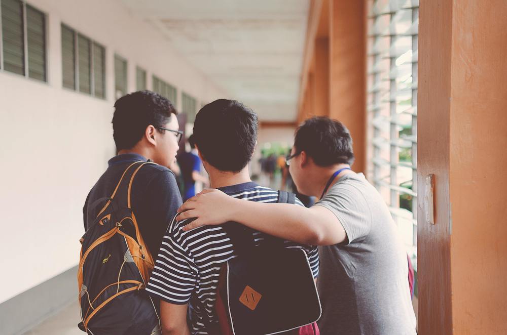 students with teacher in hallways - teacher has arm around one student - backs turned